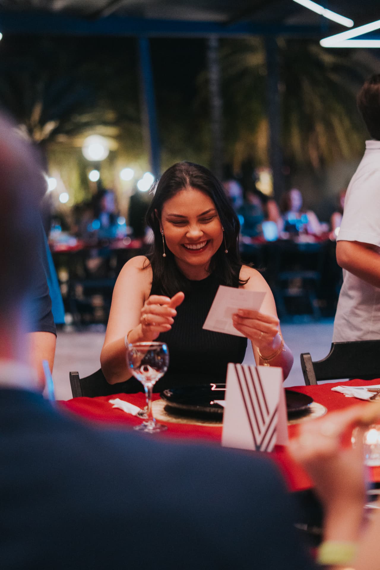 Convidada sorrindo ao ler um cartão à mesa durante um jantar do Prime Club