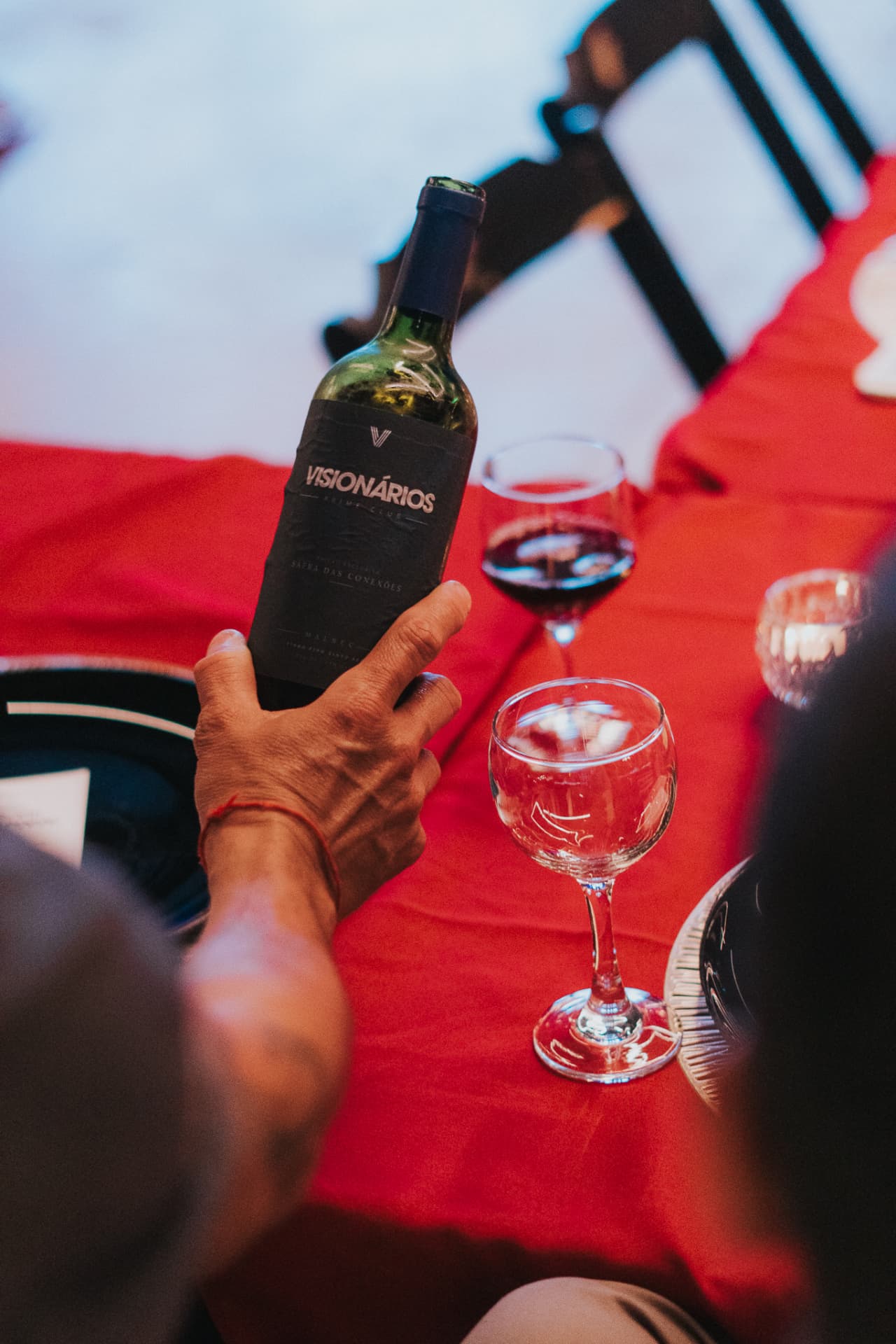 Mão servindo vinho de uma garrafa com a marca Visionários Prime Club em uma mesa de jantar