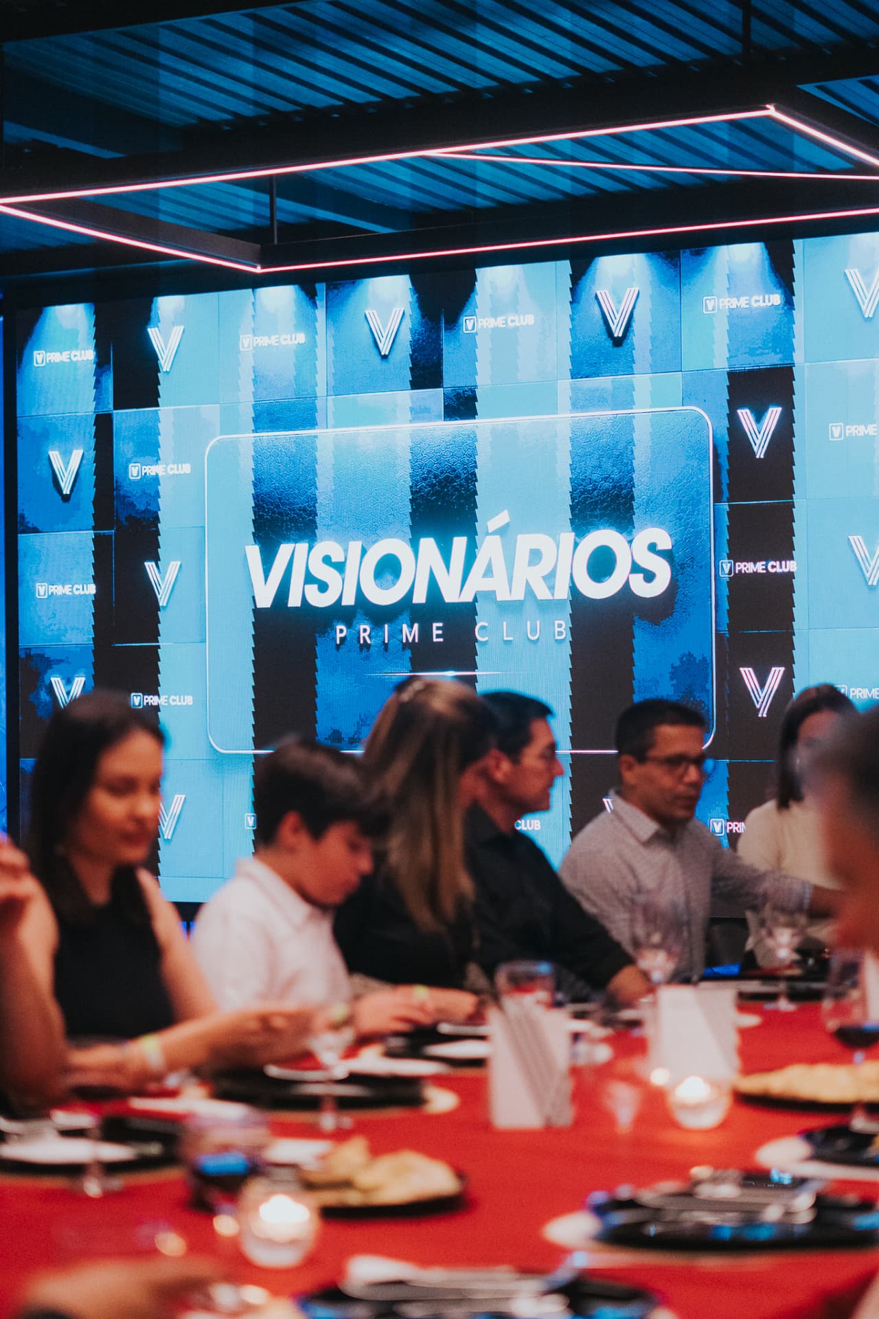 Convidados à mesa diante de um telão com a marca Visionários Prime Club